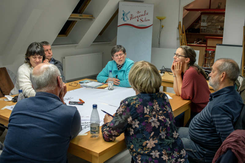 Sieben Workshop-Teilnehmer sitzen zusammen am Tisch und besprechen Ideen, die auf Papier gebracht werden sollen.