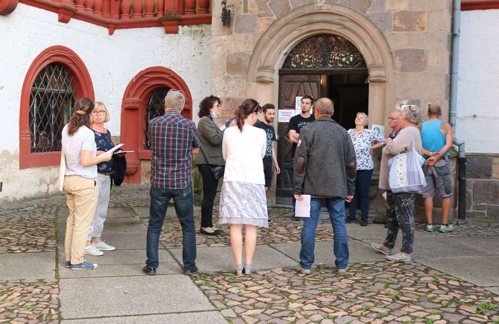 Eine Gruppe von Menschen hat sich zu einer gemeinsamen Hausbesichtigung vor dem Haupteingang von Schloss Windischleuba zusammen gefunden. Es finden mehrere Gespräch untereinander statt.