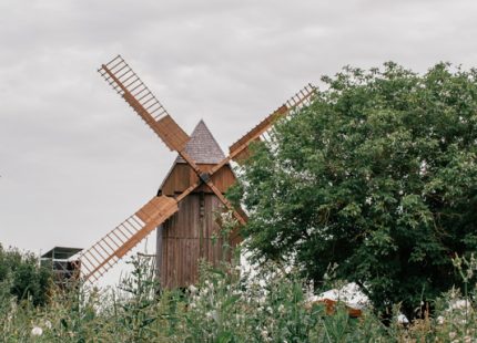 Die sehr gut erhaltene, hölzerne Bockwindmühle in Lumpzig mit allen vier Flügeln, umrahmt von grünem Idyll und wolkenverhangenem Himmel.
